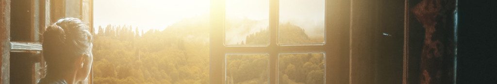 Image of a woman looking out of a window at the sun setting cc0